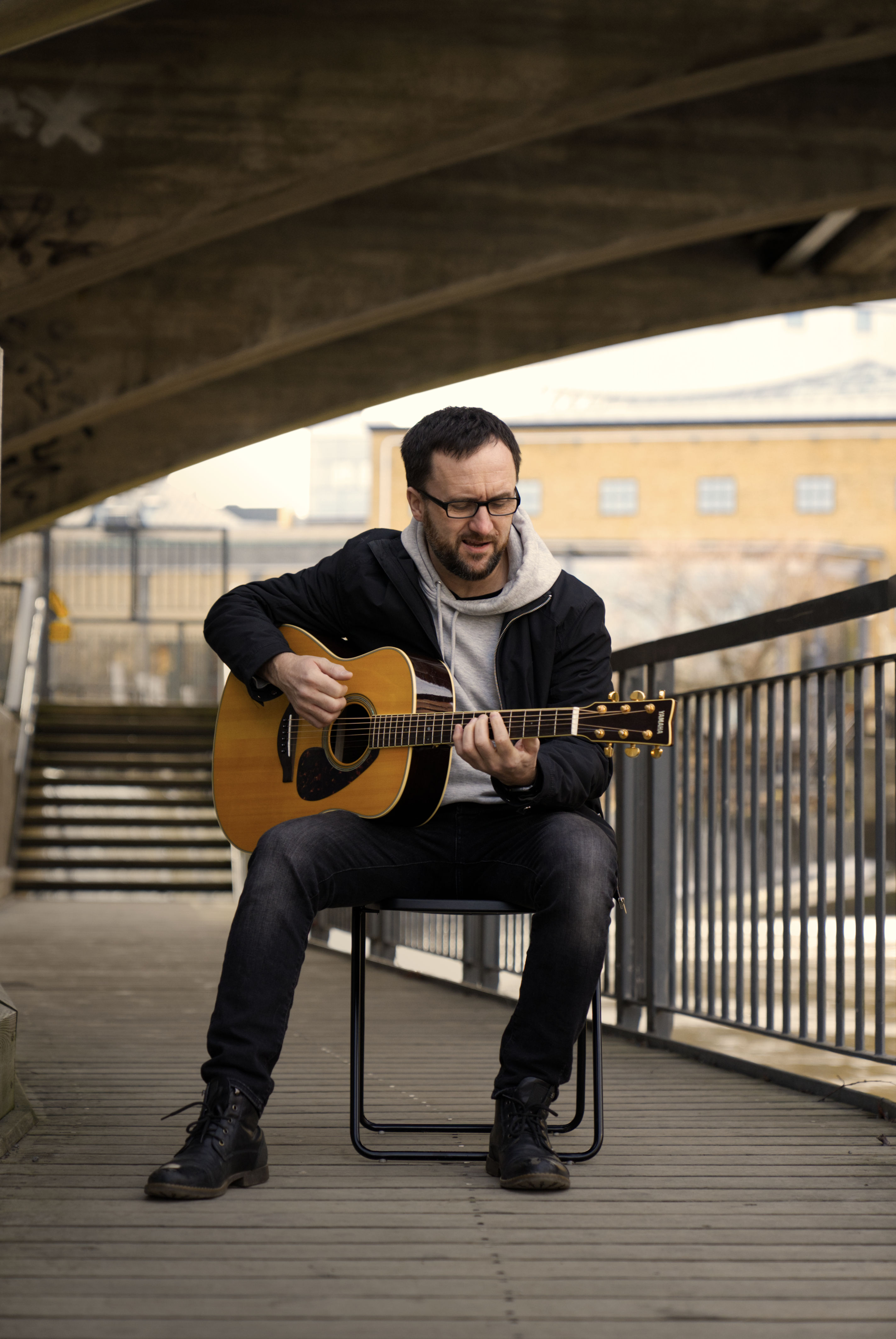 A picture taken of the artist Ola Palmkvist sitting and playing some guitar while singing